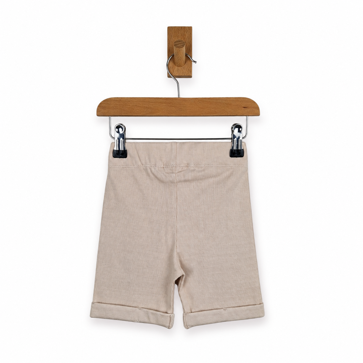 Beige ribbed knit shorts with rolled cuffs, hanging from a wooden hanger with black clips against a white background.
