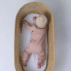 Small baby lying on her front in a wicker basket modelling pink baby romper and beanie hat
