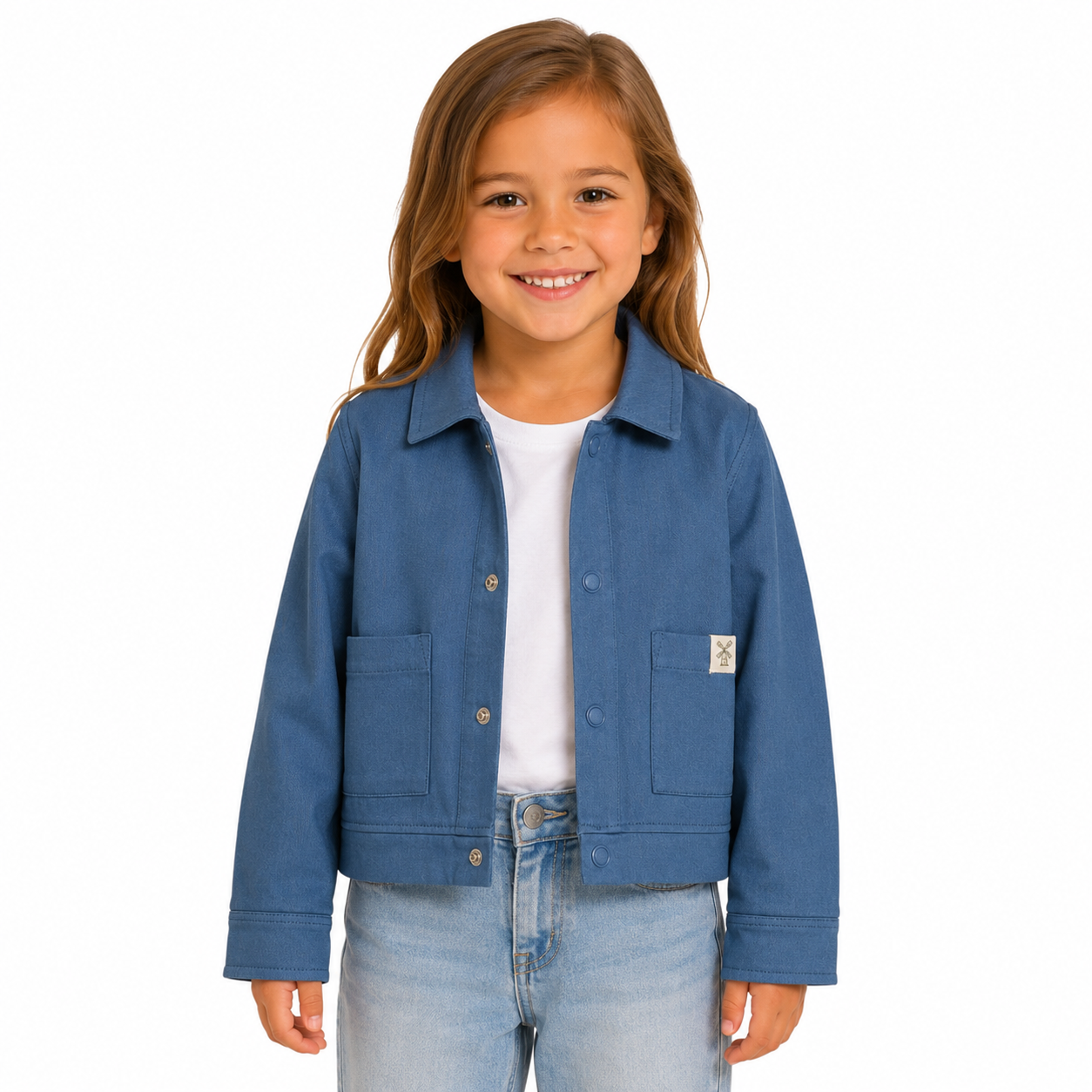 A young girl with light brown hair smiling, wearing a blue jacket over a white t-shirt and light-wash jeans, photographed against a solid white background.