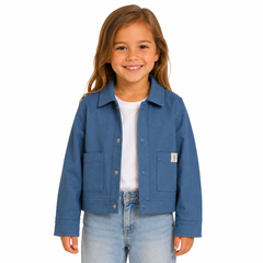 A young girl with light brown hair smiling, wearing a blue jacket over a white t-shirt and light-wash jeans, photographed against a solid white background.