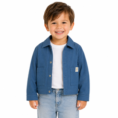 A young boy smiling, wearing a blue shacket over a white t-shirt and light blue jeans, photographed against a solid white background.