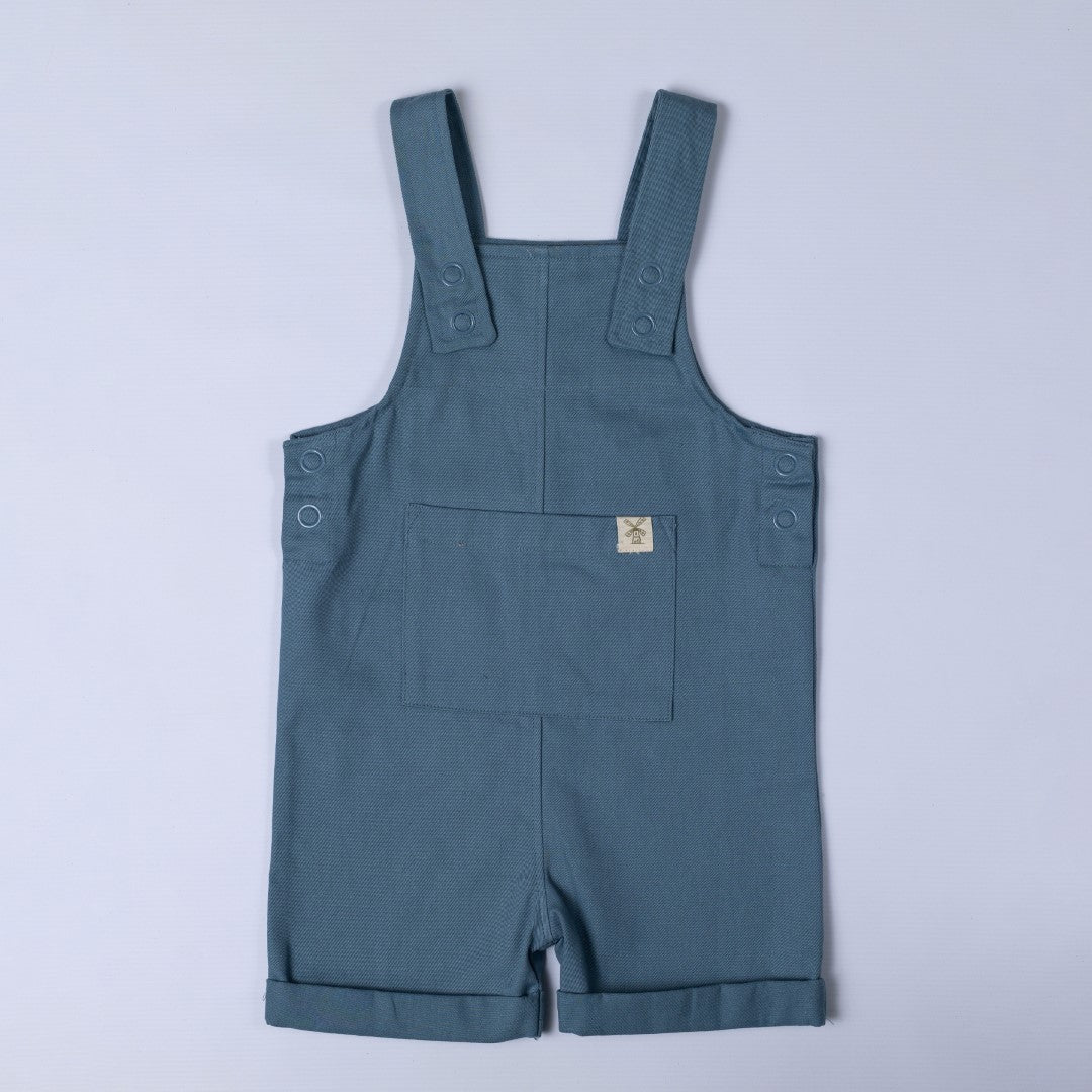 Blue dungaree shorts with a close up of the large front pocket with windmill hem tag