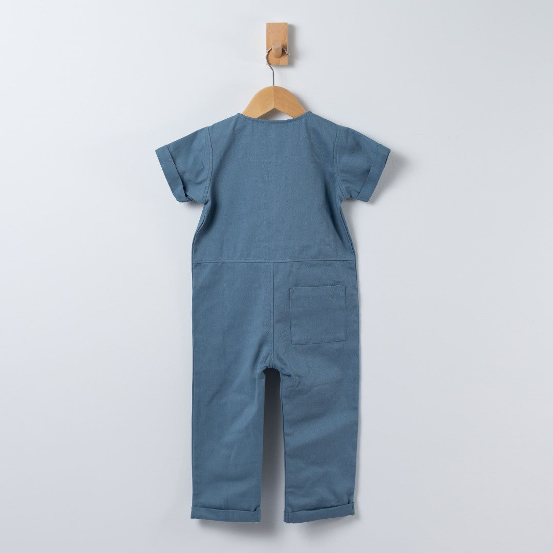 Back of slate blue jumpsuit with patch pocket on right leg and rolled hem