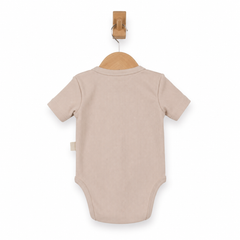 A short-sleeve baby bodysuit in a light beige color, shown from the back hanging on a wooden hanger with a wooden peg.