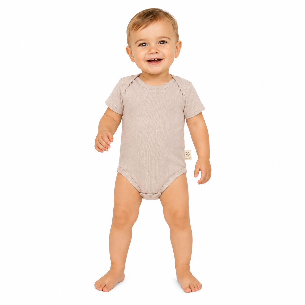 A smiling baby standing barefoot on a white background, wearing a short-sleeve, one-piece baby bodysuit in a light taupe-beige color.
