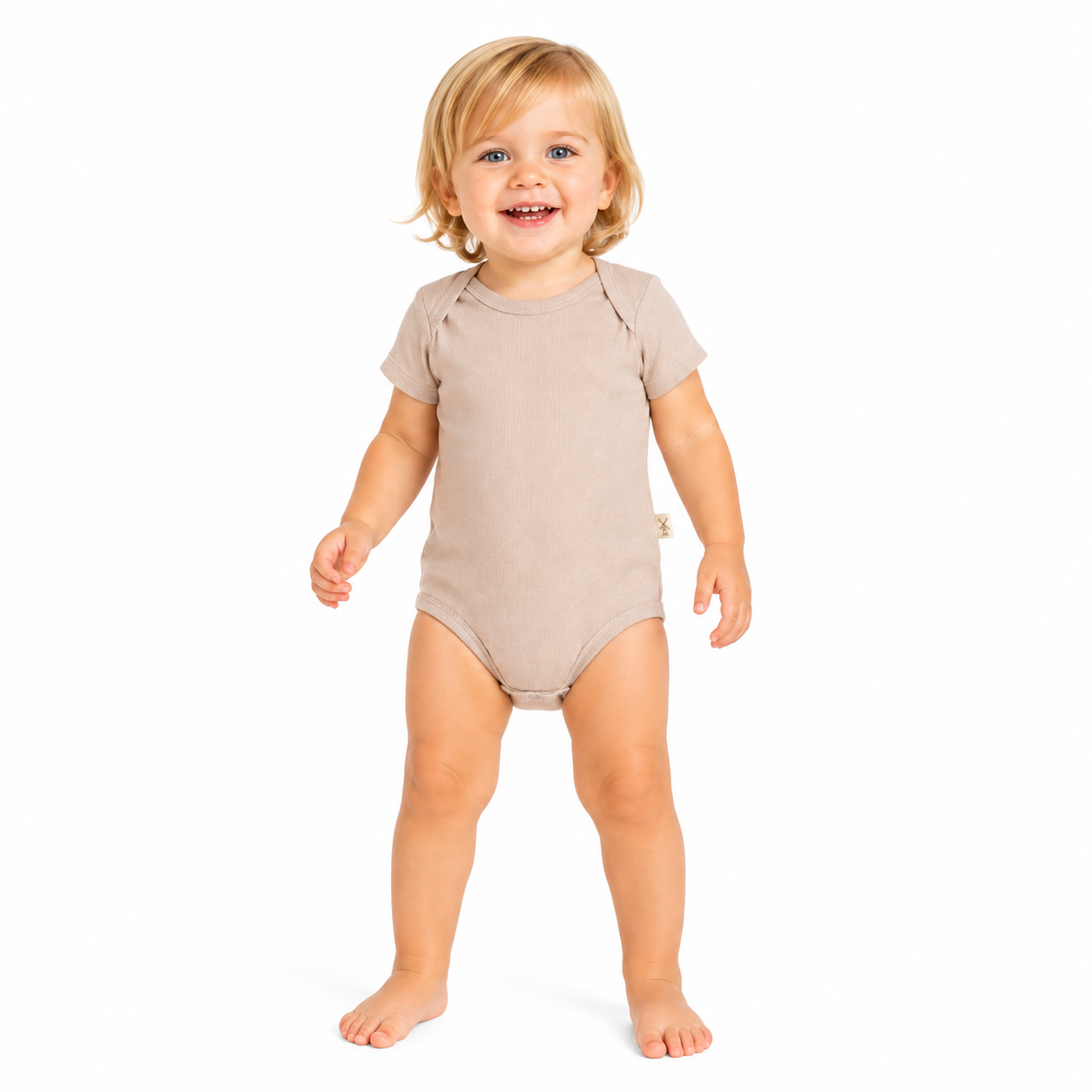 A smiling young girl standing barefoot on a white background, wearing a short-sleeve, one-piece baby bodysuit in a light beige colour.