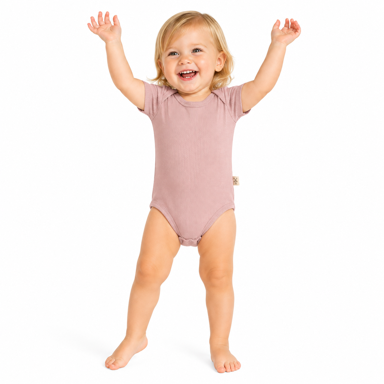 A smiling toddler with blonde hair stands barefoot on a white background, wearing a short-sleeve bodysuit in a dusty pink colour.
