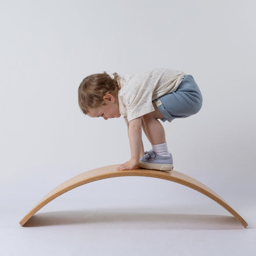 Young child standing on wooden wobble board wearing blue shorts featuring the Aneby hem tag