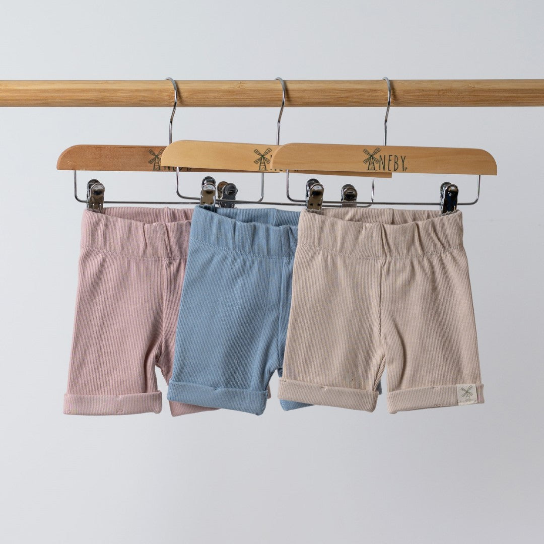 Shorts in pink,blue and beige, hanging on wooden hangers featuring the Aneby windmill logo