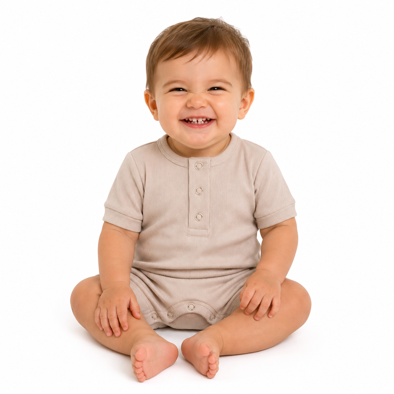 A smiling baby sitting cross-legged on a white background, wearing a short-sleeve beige romper.