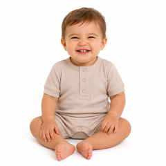 A smiling baby sitting cross-legged on a white background, wearing a short-sleeve beige romper.