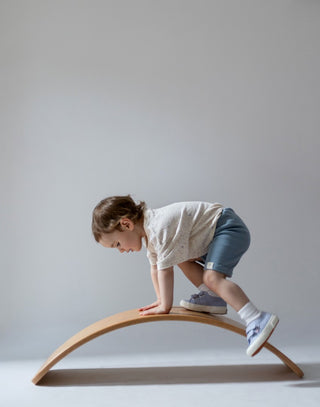 Young girl climbing on wooden arch wearing speckled cream t-shirt and blue cycle shorts