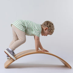 Young boy climbing on a wooden wobble board whilst modelling green and white stripey tee