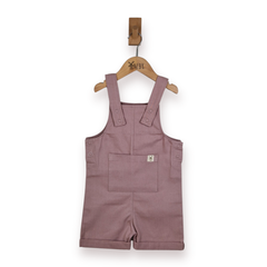A dusty rose pink children's overall romper with adjustable shoulder straps and a front pocket, hanging on a wooden hanger.