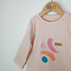 Close up of a girls dusty pink long sleeve t-shirt showing the front jersey neckline with neat edge stitching and the bold paint dash print on the front in shades of pink, mustard and turquoise.   