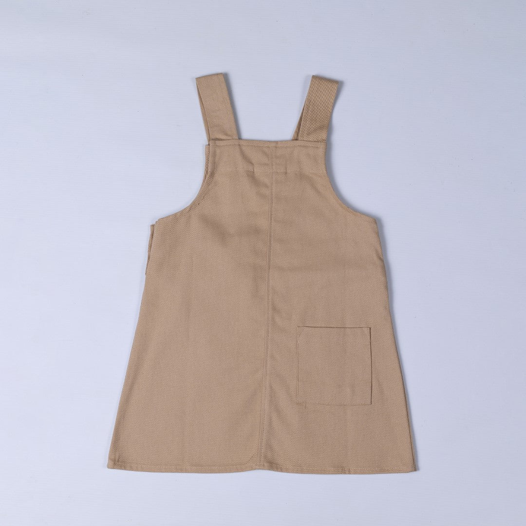 Flat lay of the back of an oat-coloured organic cotton dungaree dress, showing the crossed straps and minimalistic design.