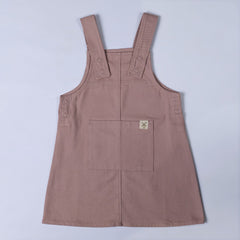 Flat lay of a dusty pink organic cotton dungaree dress, showing the front details including the pocket and buttoned straps.