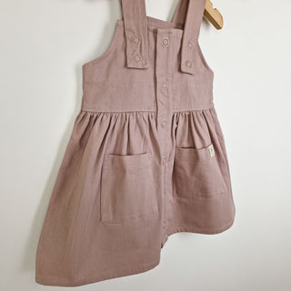 Flat lay of a dusty pink girls’ pleated dress with straps, highlighting the soft pleats and structured yet comfortable fit.
