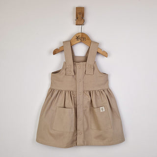 Flat lay of an oat-coloured girls’ pleated dress with straps, neatly arranged to show the full design and fabric texture.