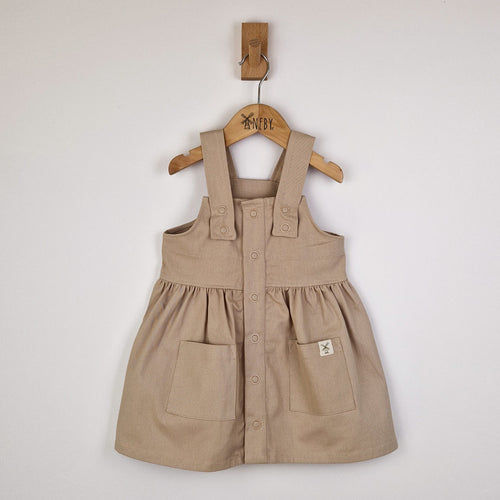 Flat lay of an oat-coloured girls’ pleated dress with straps, neatly arranged to show the full design and fabric texture.