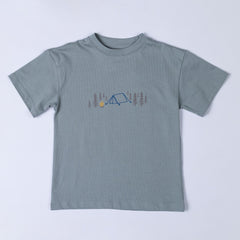 A kids' camping t-shirt laid flat, showcasing the front design. The print features a pitched tent, campfire, and fir trees on soft organic cotton fabric.