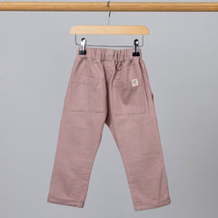 Back view of dusty pink chino-style elasticated trousers, featuring two back pockets and an Aneby hem tag, hanging from a wooden clothing frame.