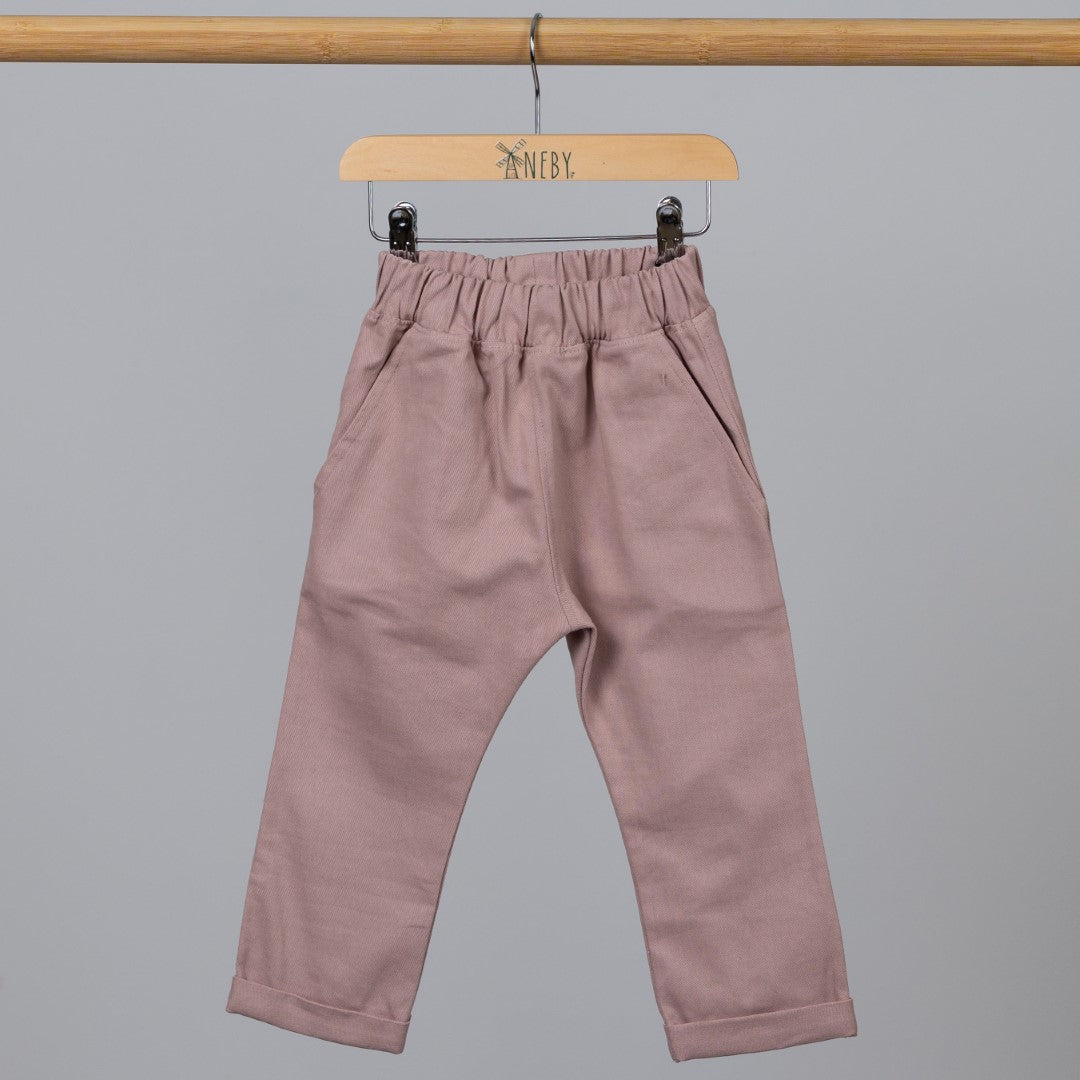 Front view of dusty pink chino-style elasticated trousers hanging from a wooden clothing frame.