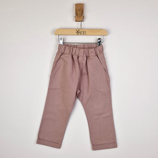 Front view of dusty pink chino-style elasticated trousers on a wooden hanger.