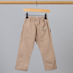 Back view of oat-coloured chino-style elasticated trousers, featuring two back pockets and an Aneby hem tag, hanging from a wooden clothing frame.