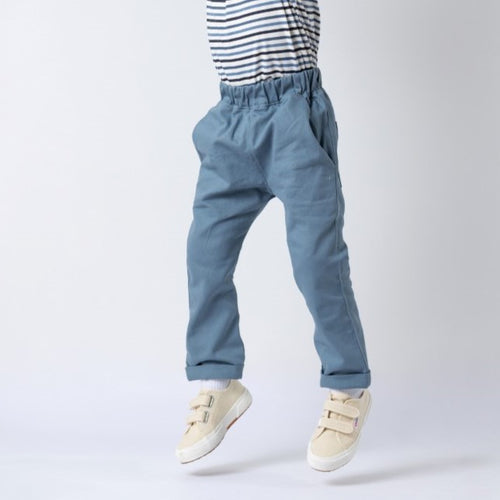 Waist-down view of a child wearing slate blue chino-style elasticated trousers, jumping with both feet off the ground against a neutral background.