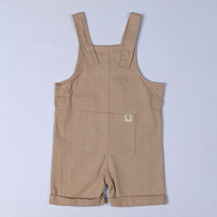 Flat lay of oat-coloured kids' cotton dungaree shorts, front view. Featuring adjustable shoulder straps, a front pocket, and a relaxed fit for all-day comfort.