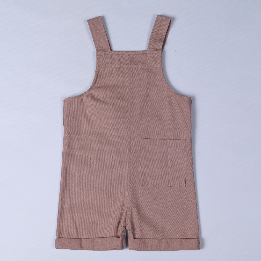 Flat lay of dusty pink kids' cotton dungaree shorts, back view. Showcasing a classic dungaree strap design with a rear pocket for added functionality.