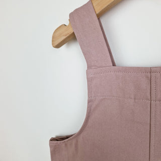Dusty pink kids' cotton dungaree shorts, back view close up. Showcasing a classic dungaree strap design with quality stitching at the centre back seam, shoulder straps and inside binding around the armhole and neckline. 