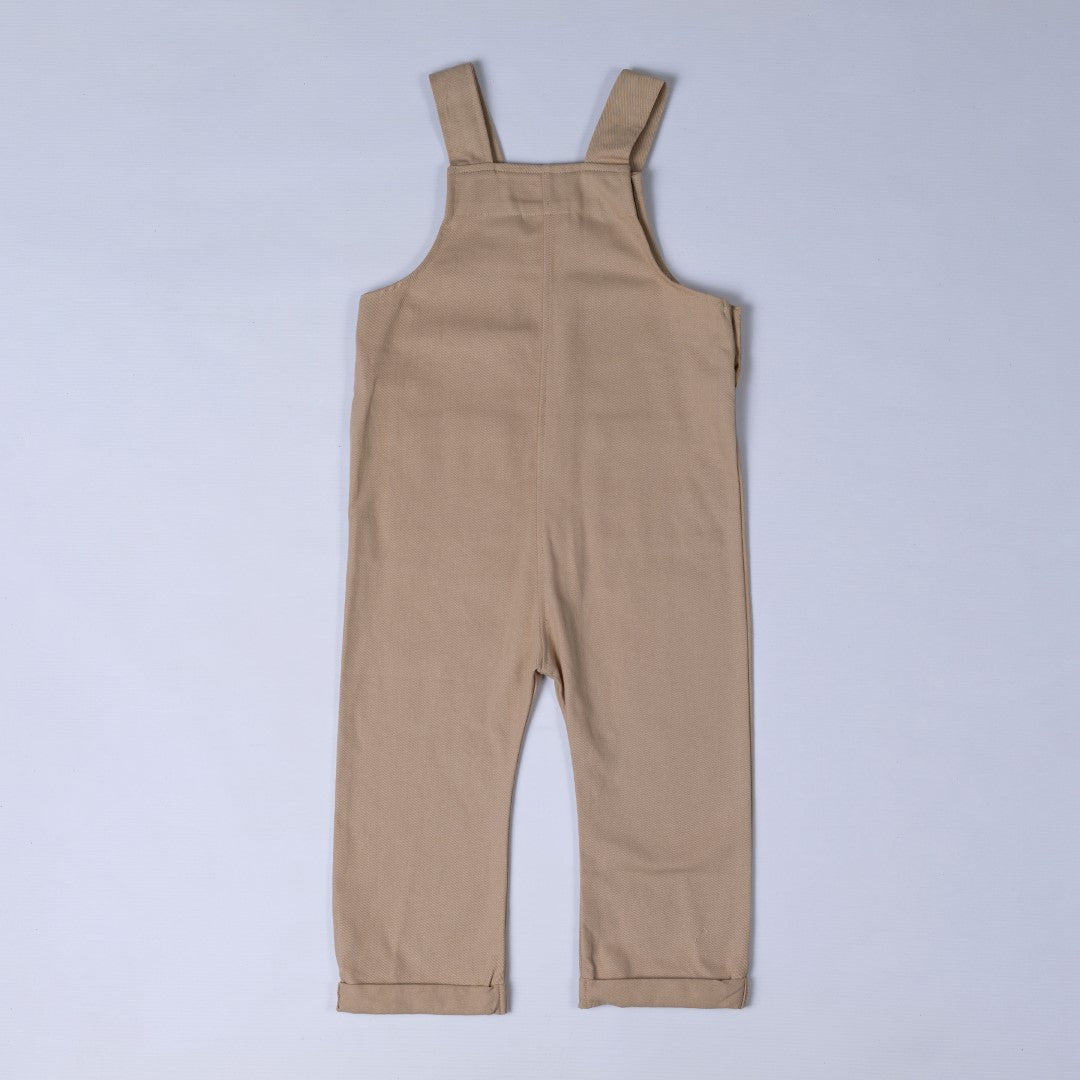 Back view of oat-coloured kids' dungarees with patch pockets, featuring a relaxed fit.