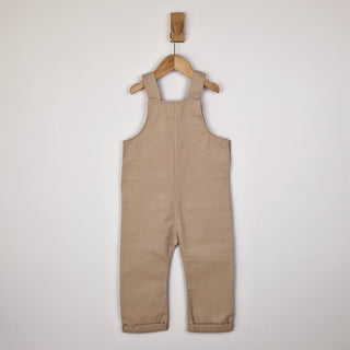 Back view of oat-coloured kids' dungarees with patch pockets, featuring a relaxed fit.