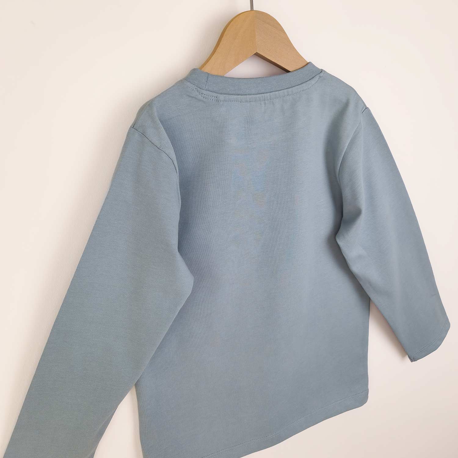 Back view of kids' long sleeve artist t-shirt. The photo shows the drop sleeve relaxed fit and the collar detail with edge stitching.