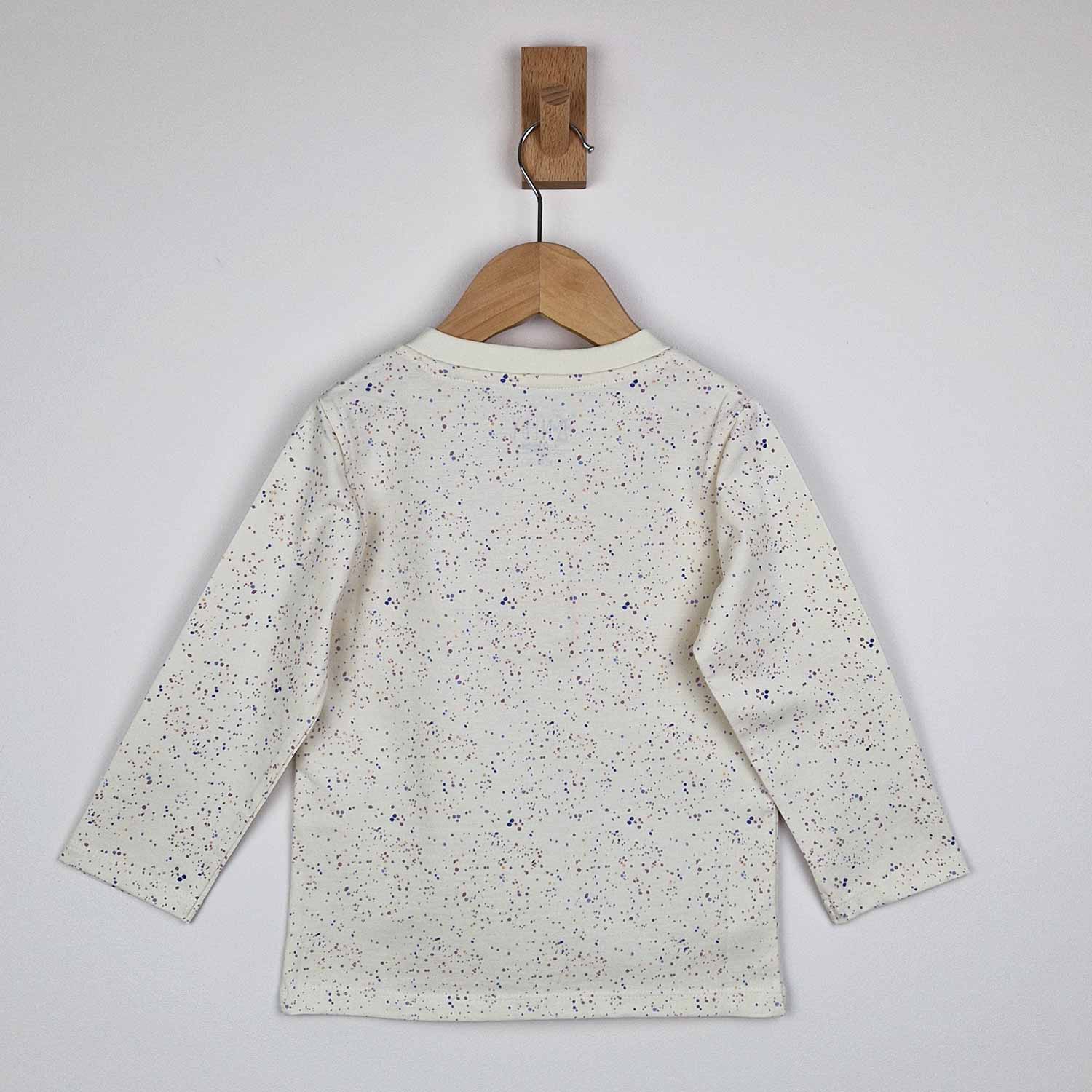 The back of a kids long sleeve ecru t-shirt on a wooden hanger showing close-up detail of the speckled print and relaxed fit on a neutral background. 