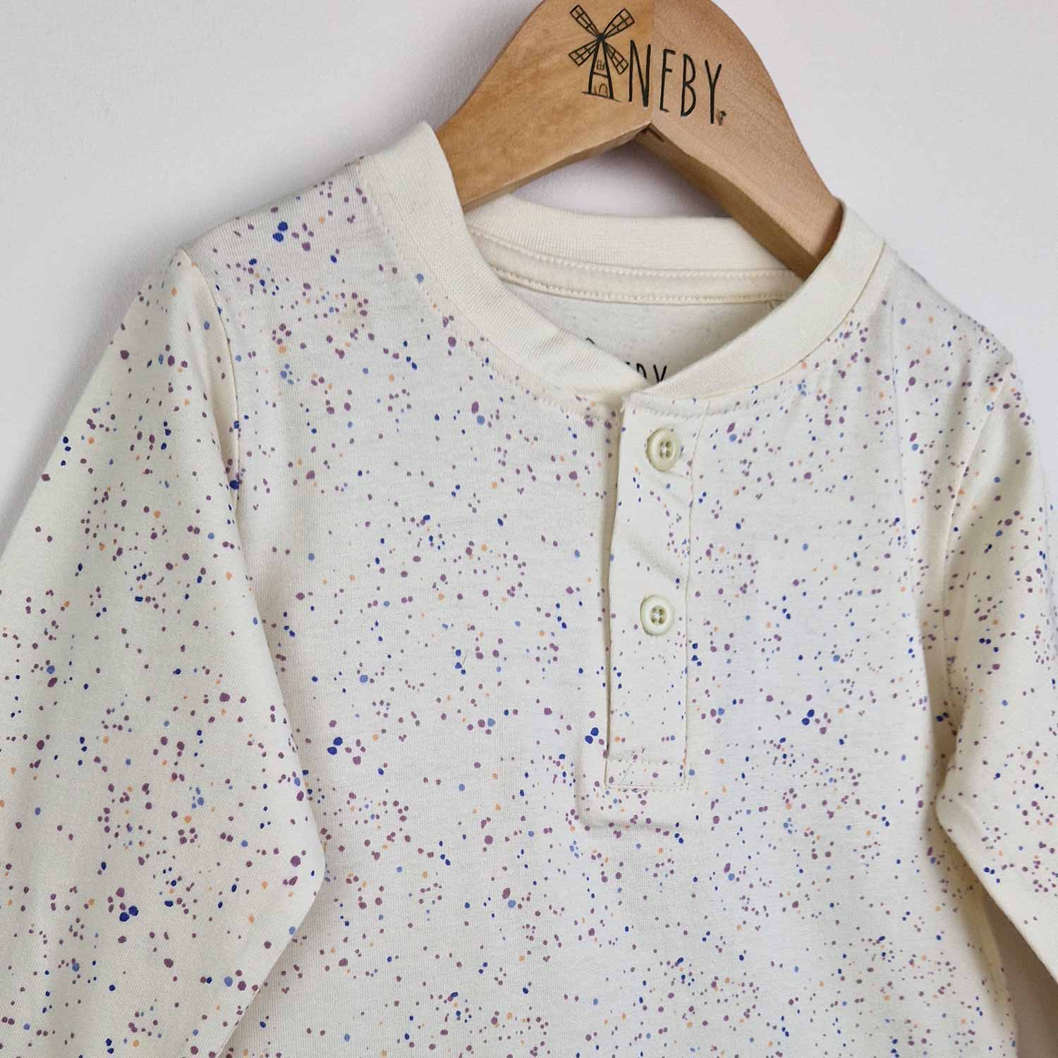 Close up photo of a kids long sleeve ecru t-shirt showing close-up detail of the speckled print and front placket opening with 2 ecru buttons.