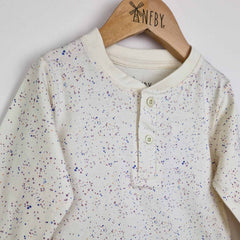 Close up photo of a kids long sleeve ecru t-shirt showing close-up detail of the speckled print and front placket opening with 2 ecru buttons.