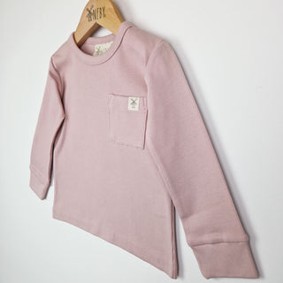 Close up front view of a dusty pink coloured kids long sleeve ribbed t-shirt on a neutral background.