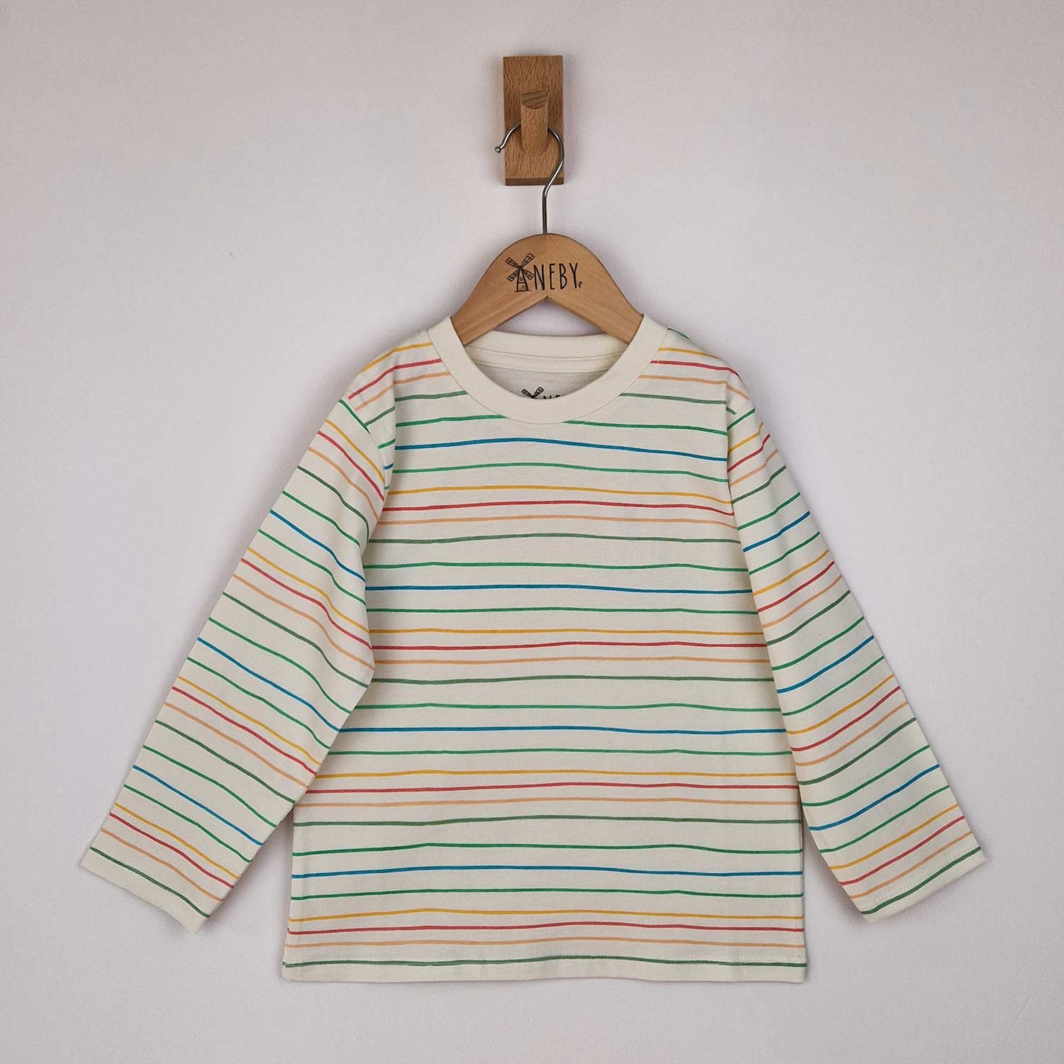 Kids long sleeve striped t-shirt with hand-drawn horizontal stripes in pastel pink, blue and yellow, hanging neatly on a wooden hanger against a neutral background.