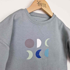 Close up of a grey kids moon sweatshirt, featuring six moons phases in blue and greige tones.