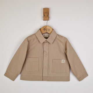 Front view of an oat-coloured kids' organic cotton shacket with a soft twill finish and front popper closure.
