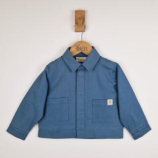 Front view of a slate blue kids' organic cotton shacket, highlighting the collar, poppers, and pocket detailing.