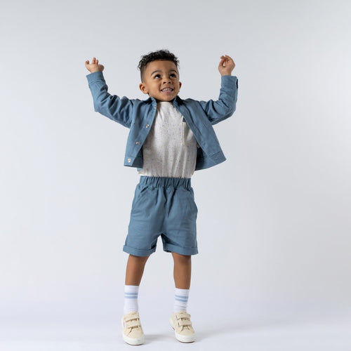 A slate blue kids' organic cotton shacket with a soft twill texture, featuring front poppers and chest pockets.