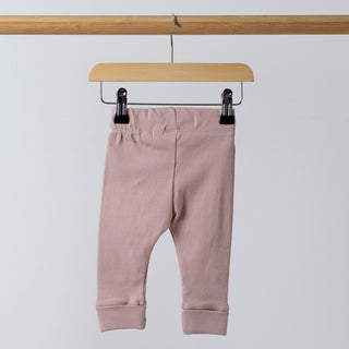 A back view of dusty pink ribbed leggings hanging from a wooden frame. The waistband and fabric texture are visible. The background is neutral, keeping the focus on the leggings.