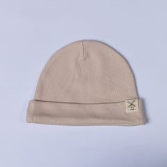 An oat-coloured kids ribbed cotton beanie hat with a fold-over cuff and a woven logo label, displayed on a white background.