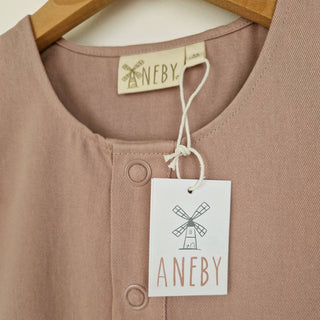 Close up image of the front neckline of a dusty pink short sleeve overall hanging on a wooden hanger.