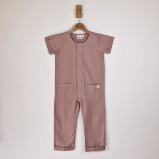Dusty pink short-sleeve overall hanging on a wooden hanger with a front view in a neutral background.