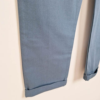 Close up image of the leg and rolled hem of a slate blue short sleeve overall on a neutral background.